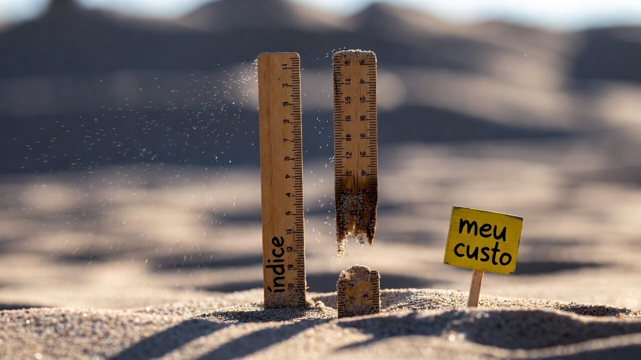 Duas réguas de madeira fincadas na areia: uma intacta e a outra visivelmente corroída e mais curta